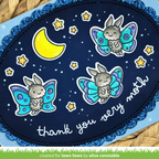 A close-up of a handmade oval card featuring three cartoon rabbits with colorful wings, a yellow crescent moon, stars, and the phrase 'thank you very moth' on a dark blue background with glittery blue scalloped edges. | color-code:alt1