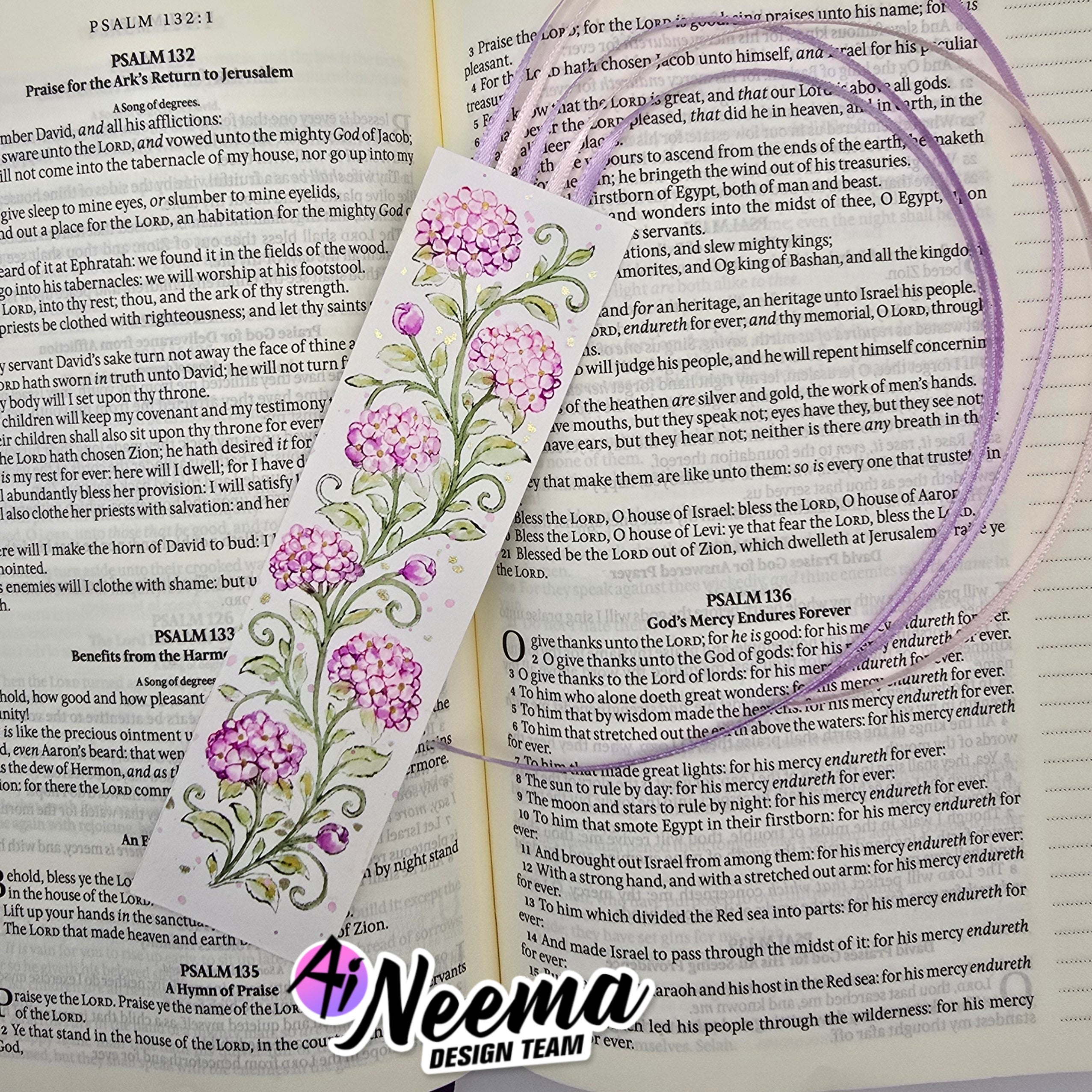 A decorative Bible bookmark featuring a purple and lavender floral vine design with green leaves and white scrollwork, laid over an open book with printed text.