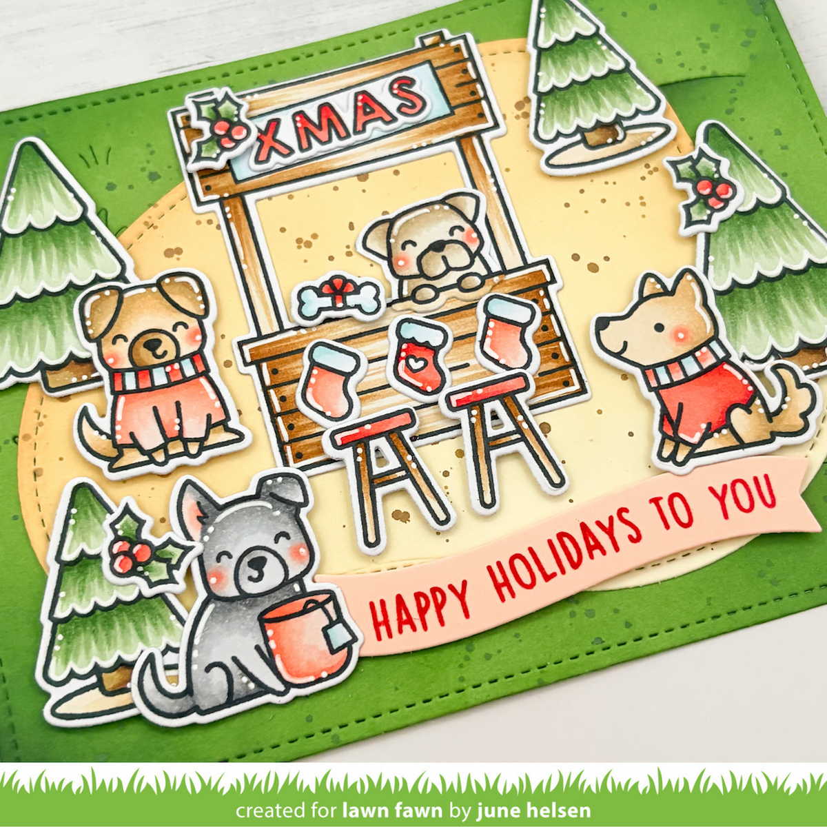 A handmade Christmas-themed card featuring cartoon dogs around a wooden Xmas stall, with red stockings, green trees, and a pink banner reading “HAPPY HOLIDAYS TO YOU.”.