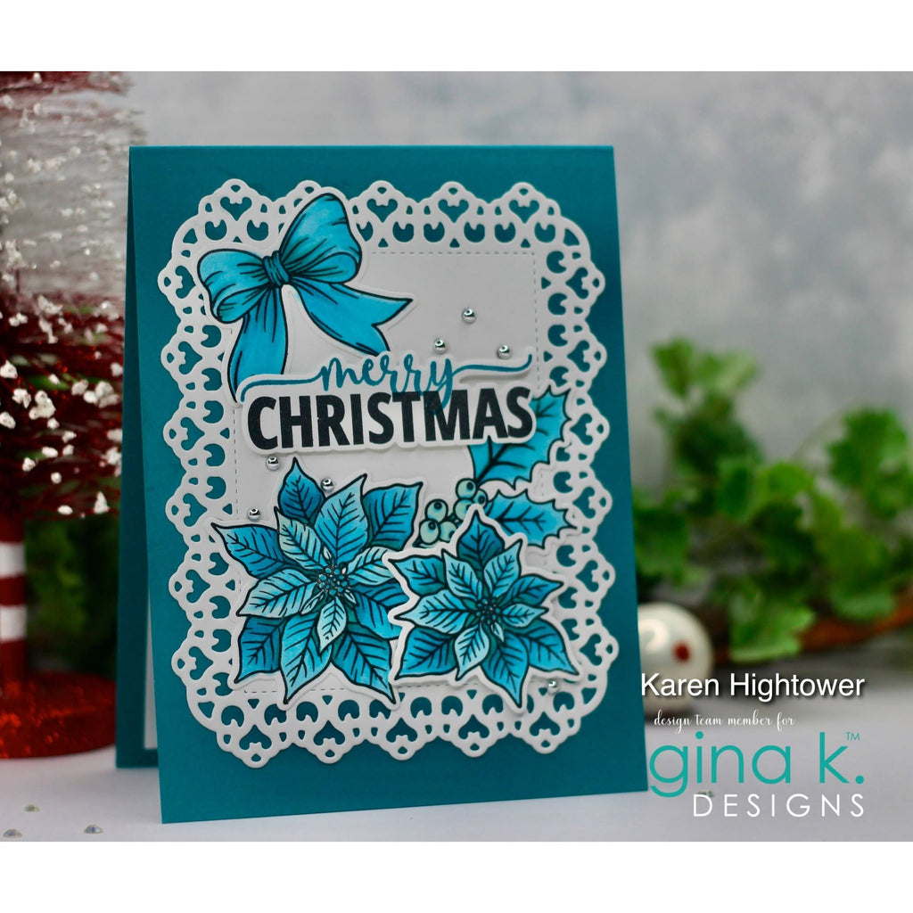 A handmade Christmas greeting card featuring a teal background, a white scalloped die-cut border, a turquoise bow, poinsettia flowers, and the words 'merry CHRISTMAS' in black script and block lettering. The card is photographed on a tabletop with blurred holiday decorations and greenery in the background.