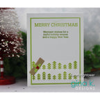 A handmade Christmas greeting card with green text reading 'MERRY CHRISTMAS' and a holiday message, decorated with green pine tree stamps and a small brown envelope with a red holly accent. The card is displayed on a white surface with blurred festive decorations in the background.