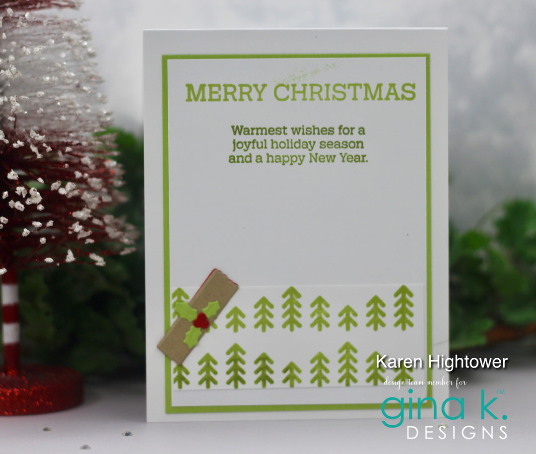 A handmade Christmas greeting card with green text reading 'MERRY CHRISTMAS' and a holiday message, decorated with green pine tree stamps and a small brown envelope with a red holly accent. The card is displayed on a white surface with blurred festive decorations in the background.