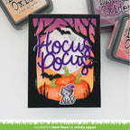 A handmade Halloween-themed card featuring layered black, purple, orange, and pink elements, including the words 'Hocus Pocus' in purple script over pumpkins, bats, a full moon, and a small cat sticker. Surrounding stamps are partially visible on a white surface. | color-code:alt1
