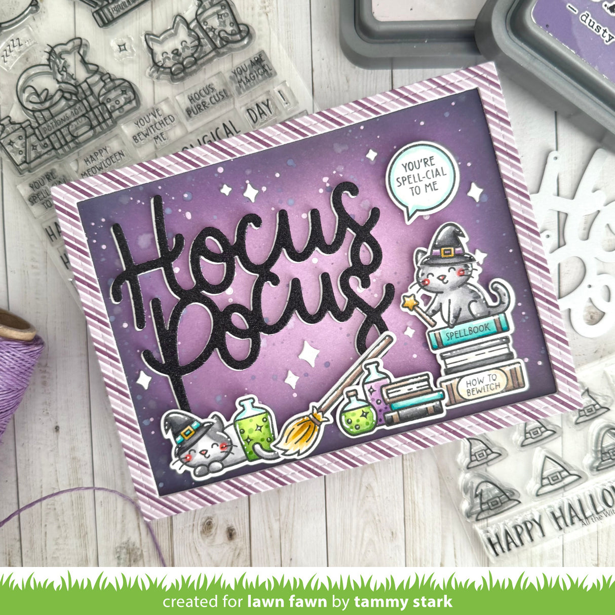 A handmade Halloween-themed card with a purple and lavender background, featuring the words 'Hocus Pocus' in large black script, a white cat dressed as a witch sitting on books, potion bottles, and a speech bubble that says 'YOU'RE SPELLICAL TO ME.'