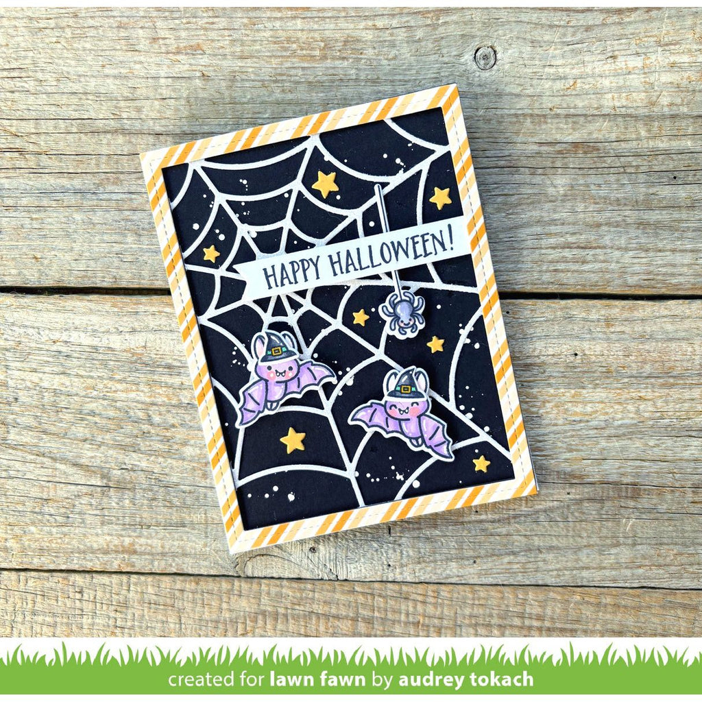 A handmade Halloween greeting card featuring cute purple bats, a spider, and stars on a black background with a spiderweb pattern and orange-and-white striped border.