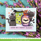 A handmade Halloween greeting card featuring two cartoon gray cats, a green slime jar, a purple potion bottle, and a pink banner reading 'Wishing you a Purrfect Halloween.' The card is displayed on a turquoise surface surrounded by purple flowers. | color-code:alt2