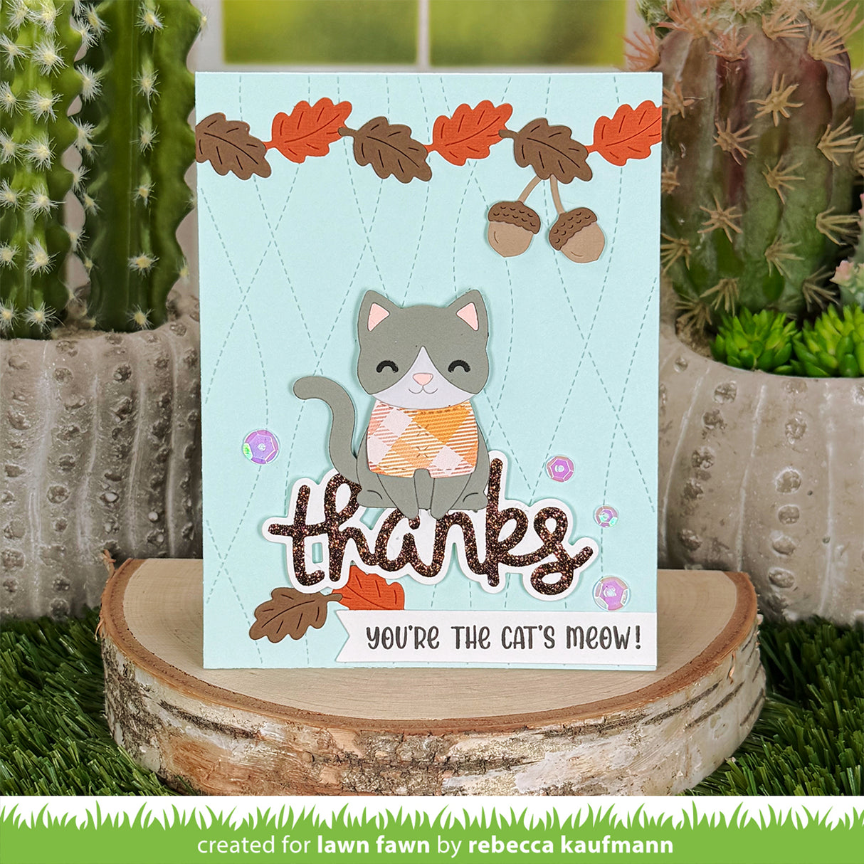 A handmade autumn-themed greeting card featuring a cute gray cat with an orange patterned sweater, acorns, and the words 'thanks' and 'you're the cat's meow!'