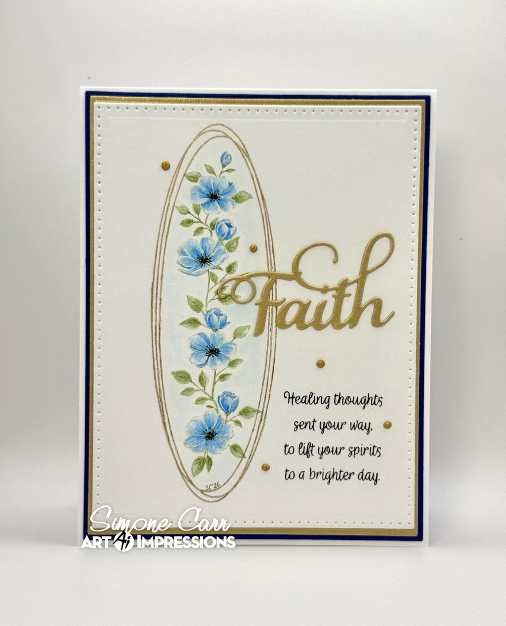 A handmade greeting card featuring a cream background, a navy blue border, a gold oval frame, blue flowers, green leaves, and the word 'Faith' in gold script. 