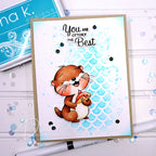 A handmade greeting card featuring a cute cartoon otter holding a gift box, with the text 'You are OTTERLY The Best' above it. The card has a light blue scalloped background and is photographed on a white surface with craft supplies nearby.