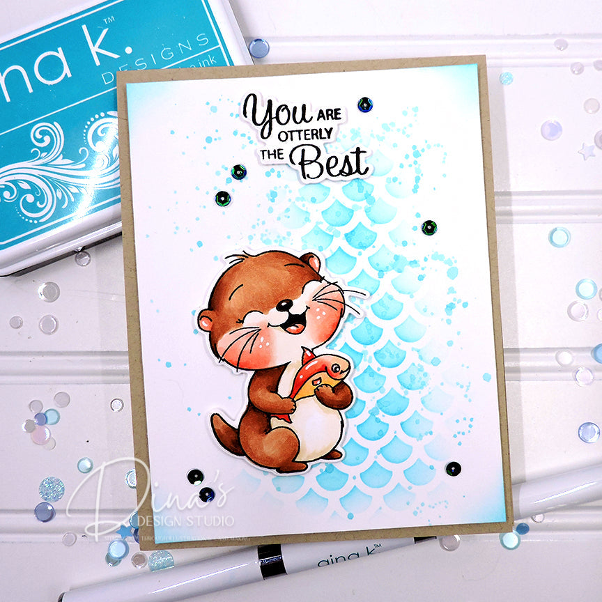A handmade greeting card featuring a cute cartoon otter holding a gift box, with the text 'You are OTTERLY The Best' above it. The card has a light blue scalloped background and is photographed on a white surface with craft supplies nearby.