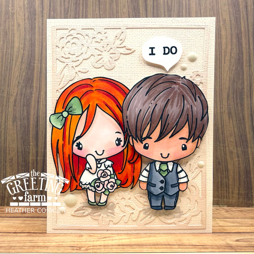 A handmade greeting card featuring a cute chibi-style couple with a speech bubble that says 'I DO'. The card is displayed on a wooden surface with a wood-grain background.