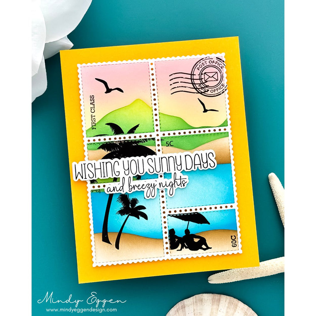 A handmade greeting card featuring a postage stamp collage design with beach scenes and the text 'WISHING YOU SUNNY DAYS and breezy nights,' photographed on a teal surface with decorative seashells and a white flower.