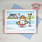 A handmade greeting card featuring a winter scene with a snowman wearing a hat and scarf, surrounded by small birds, with the text 'FROSTY friends'. The card is displayed on top of a blue envelope on a light wood background, with branding for 'The Greeting Farm' visible.