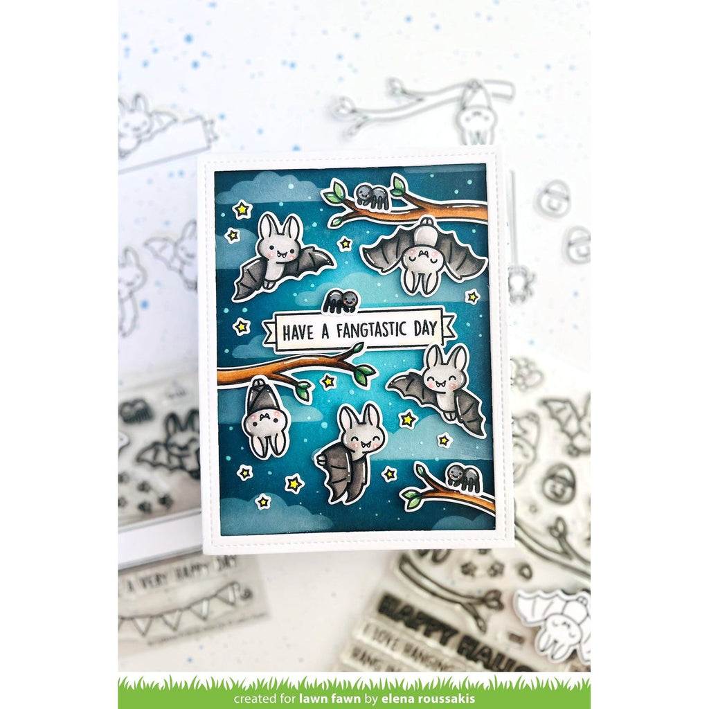 A handmade greeting card featuring cute cartoon bats flying on branches against a blue starry night sky, with the text 'HAVE A FANTASTIC DAY'. The card is displayed on a white surface with clear stamp designs in the background.