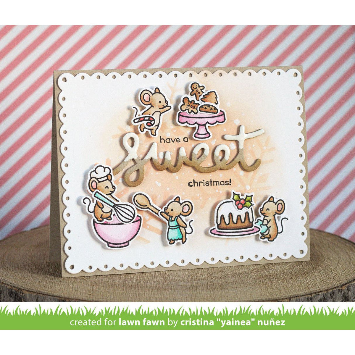 A handmade greeting card featuring cute cartoon mice baking and decorating cakes, with the text 'have a sweet christmas!'. The card is displayed on a wooden slice with a pink and white striped background.