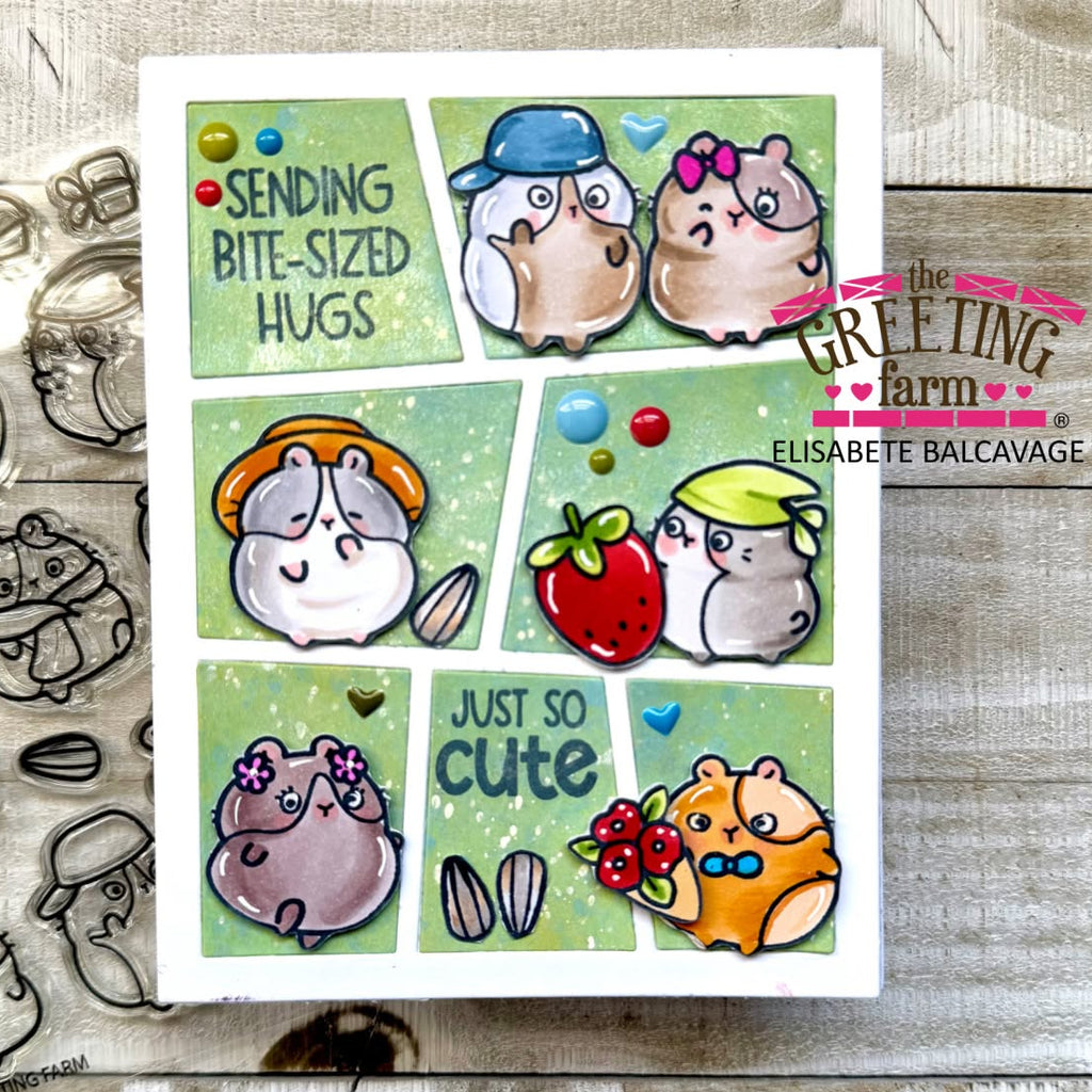A handmade greeting card featuring six comic-style panels with cute hamsters in different outfits and expressions, accompanied by small decorative elements like a strawberry, mushrooms, and hearts. The card is displayed on a rustic wood surface with clear stamp designs visible around it.