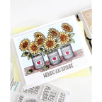 A handmade greeting card featuring three potted sunflowers with the text 'WISHING YOU SUNSHINE' on a white background, styled with crafting tools and stamps.