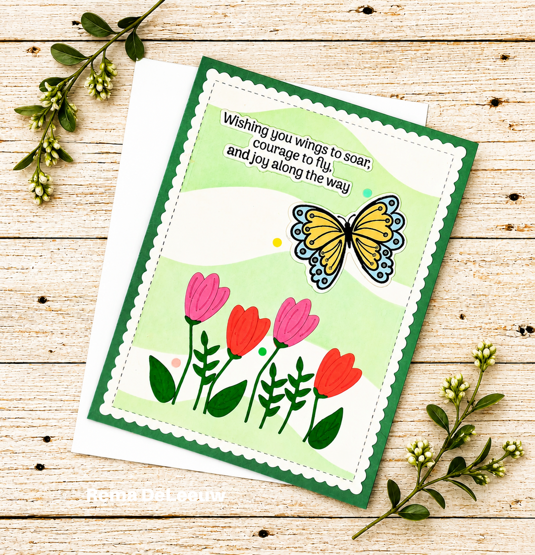 A handmade greeting card with a green border, scalloped white edge, a yellow butterfly, pink and red tulips, and a quote, displayed on a white envelope over a light wood background with green sprigs.