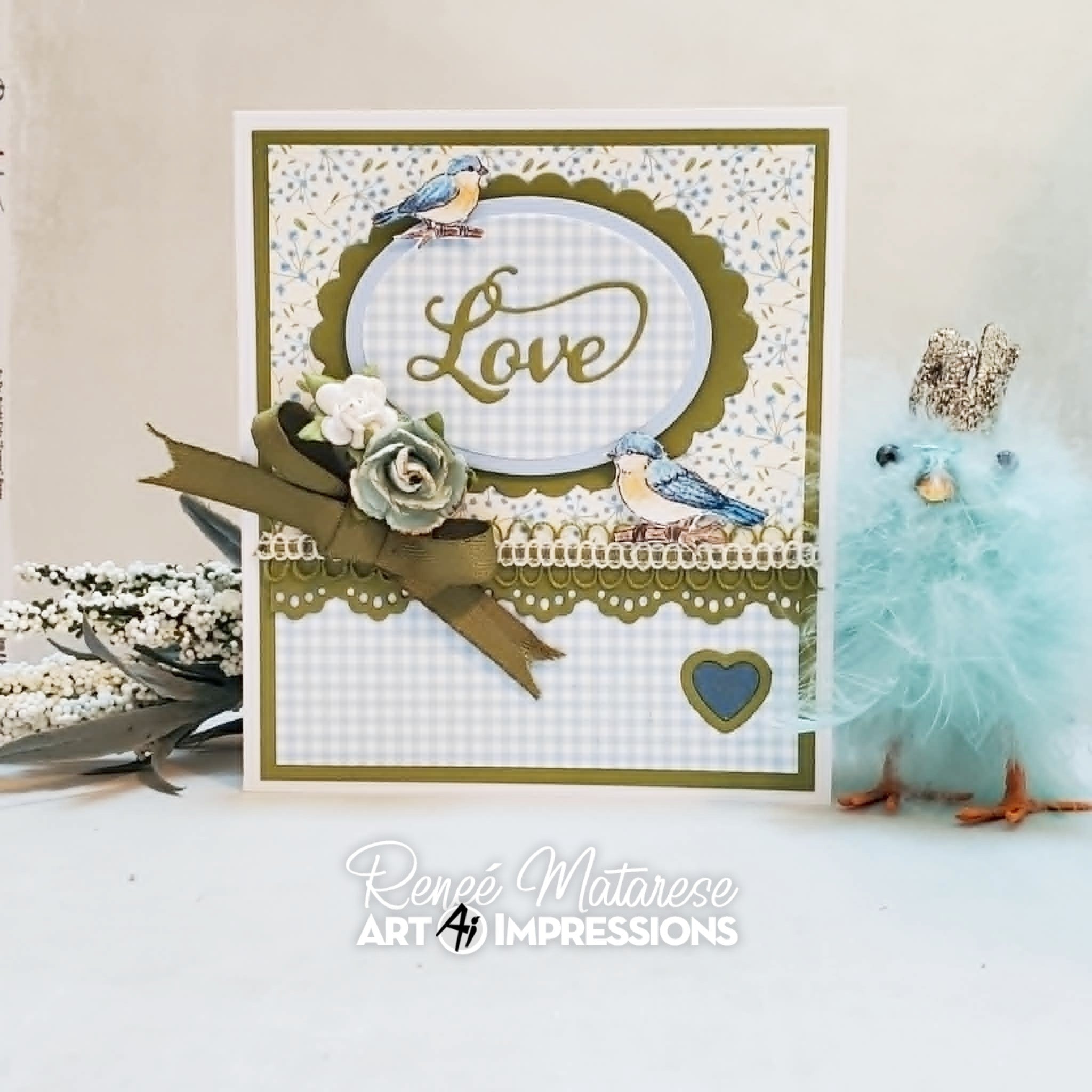 A handmade greeting card with a white and beige gingham pattern, olive green scalloped borders, blue birds, and a large olive green ribbon bow with a rose. 