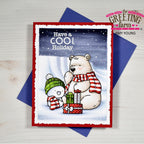 A handmade holiday greeting card from The Greeting Farm by Amy Young, featuring a cute cartoon polar bear and snowman with presents under a snowy night sky. The card is displayed on top of a blue envelope on a light wood background.