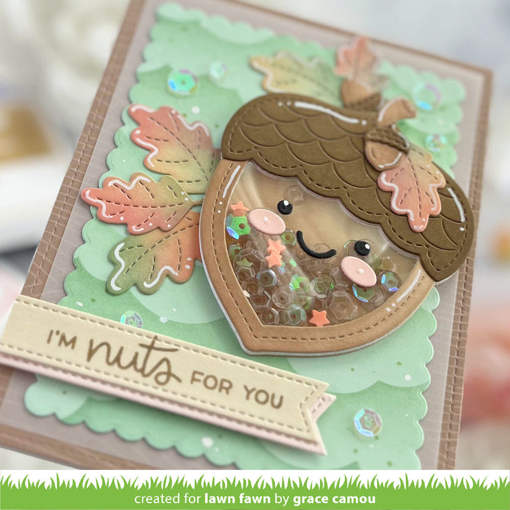 A handmade layered card featuring a cute acorn face with sequins inside, autumn leaves, and a banner that reads 'I'M nuts FOR YOU'.