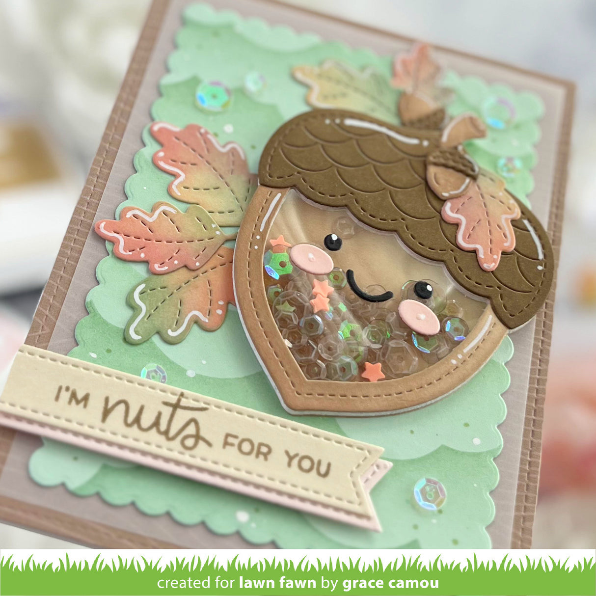 A handmade layered card featuring a cute acorn face with sequins inside, autumn leaves, and a banner that reads 'I'M nuts FOR YOU'.