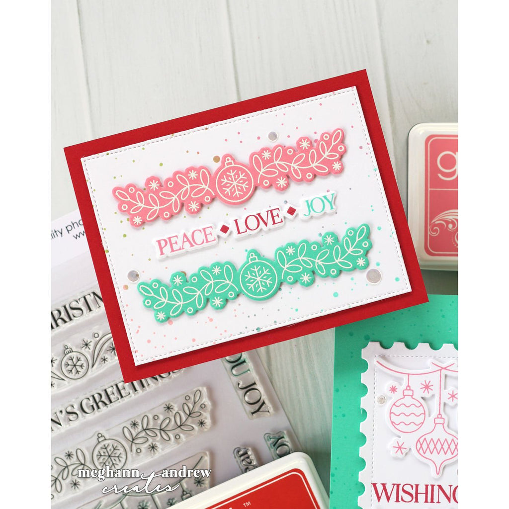 A handmade layered card featuring a red border, a pink holiday garland with snowflakes and ornaments, and a green garland with ornaments and snowflakes. The card has the words 'PEACE', 'LOVE', and 'JOY' layered in the center.