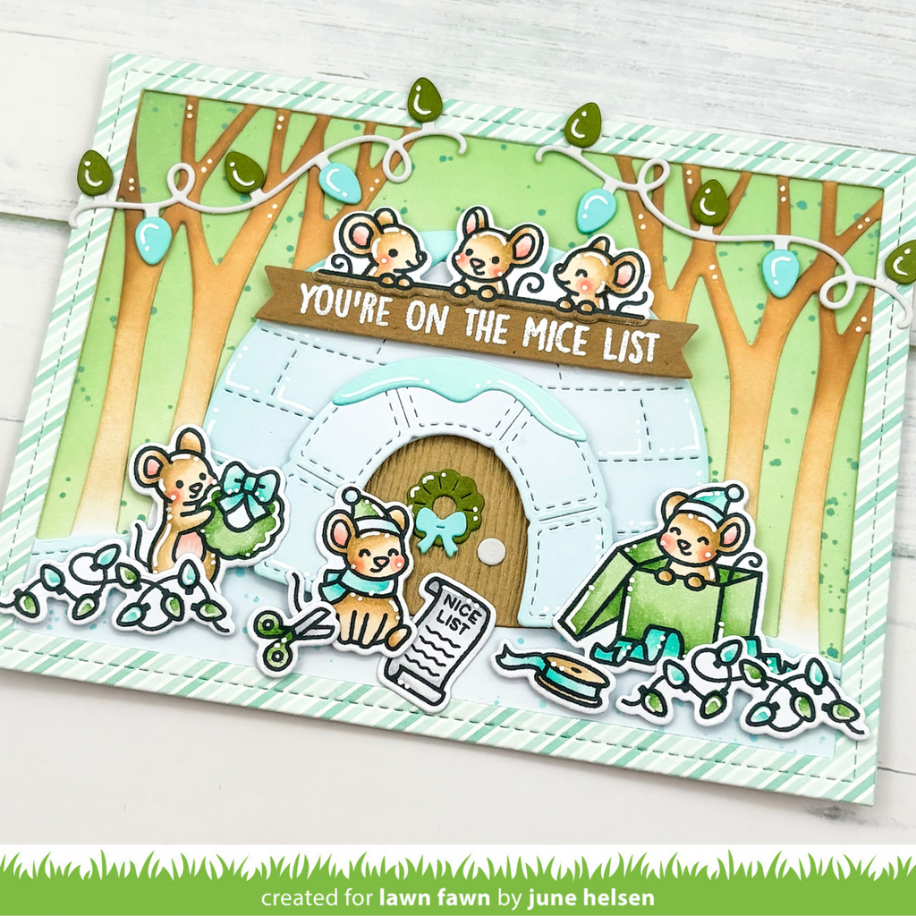 A handmade layered card featuring cute cartoon mice around a small white igloo with a wooden door and a brown banner reading 'YOU'RE ON THE MICE LIST'. The card includes green striped borders, string lights, trees, and small die-cut mouse decorations, photographed on a white wood surface.