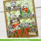 A handmade layered card featuring four illustrated puppy tea-time scenes with pinecones, snowflakes, candy canes, and the phrase 'YOU'RE MY pup OF TEA'. The card is photographed on a white wood background with a green grass-like strip at the bottom reading 'created for lawn fawn by june helsen'.