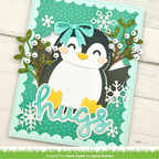A handmade layered greeting card featuring a penguin with a teal bow, surrounded by greenery, white snowflakes, and the word 'hugs' in teal script. The card is photographed on a white wood background with a green grass banner at the bottom reading 'created for lawn fawn by june helsen'.