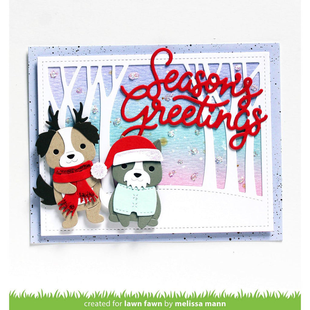 A handmade layered greeting card with two cute dog cutouts wearing Santa hats and scarves, set against a pastel winter forest background with red cursive 'Seasons Greetings' text. A green strip at the bottom reads 'created for lawn fawn by melissa mann'.