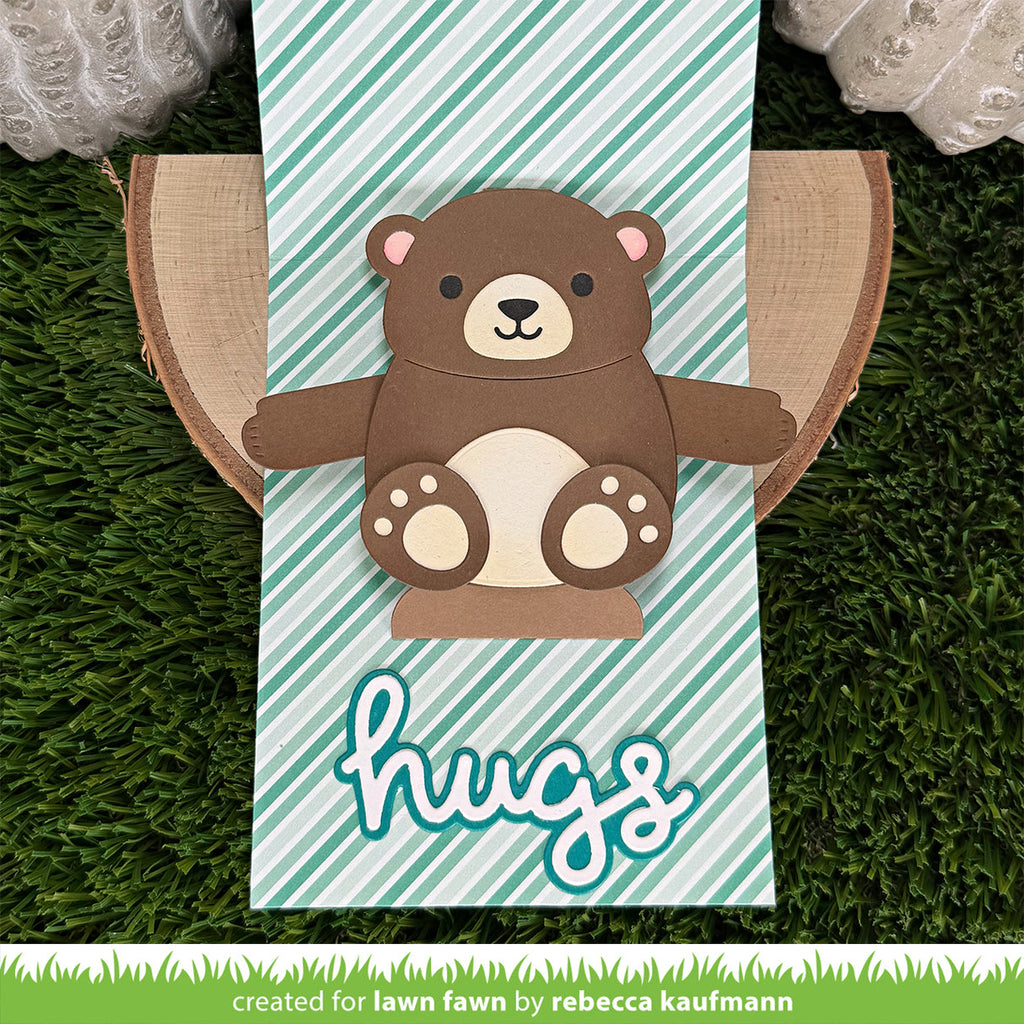 A handmade paper craft card featuring a cute brown bear with a cream snout and paws, set against a mint green and white striped background with the word 'hugs' in white script. 