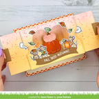 A handmade pop-up card art piece with autumn themes, held open by two hands. The design features a 3D pumpkin, cartoon mice, fall leaves, and the text 'FALL INTO AUTUMN!' on a warm orange and yellow gradient background with speckles and scalloped trim.