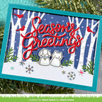 A handmade square greeting card with a winter forest scene, featuring the words 'Season's Greetings' in red script, two small white dog and cat figures, red birds, and snowflake embellishments. The card is styled with green pine branches in the background.
