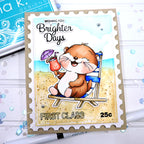 A postage stamp-style greeting card featuring a cartoon brown bear sitting on a beach chair at the beach, holding a cocktail umbrella. The card has scalloped edges, a kraft paper border, and the text 'Wishing You Brighter Days' and 'First Class 25c'.