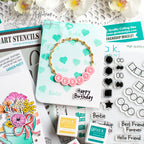 A styled flat-lay of crafting supplies and a handmade friendship bracelet. The central product is a gold-tone circular charm bracelet with pink round beads spelling 'BESTIE' and a black stamped 'Happy Birthday'