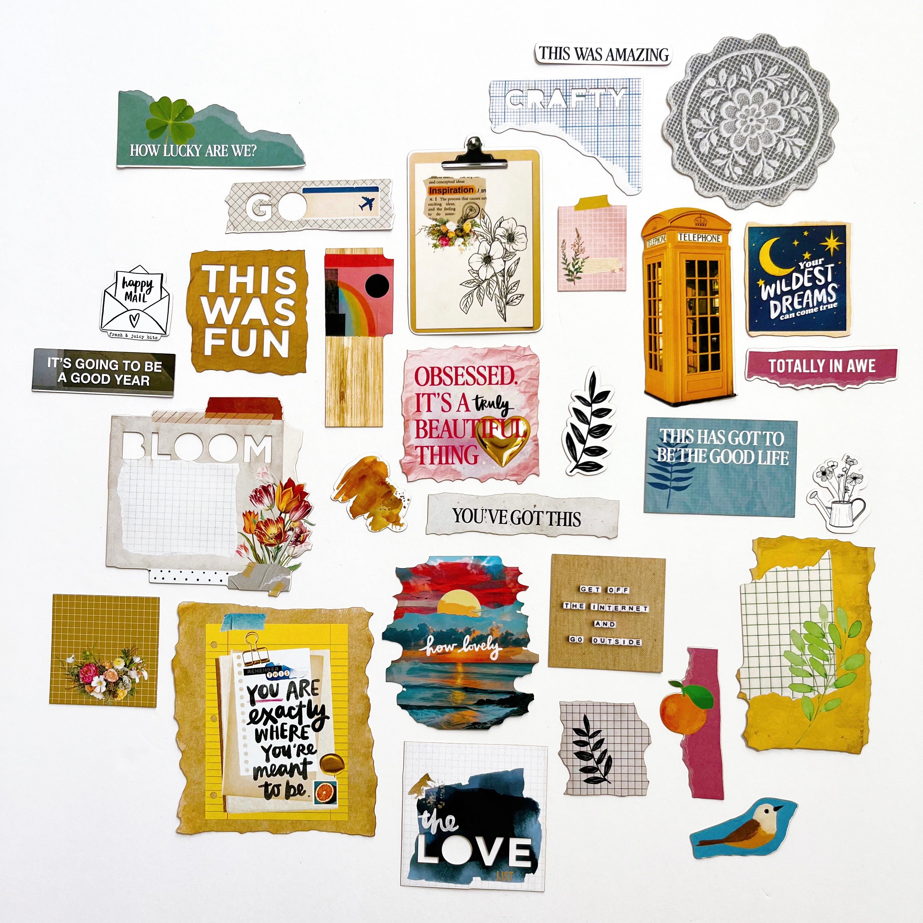 A flat-lay collection of various scrapbook paper sheets, stickers, and embellishments with inspirational quotes, floral designs, patterns, and colorful accents on a clean white background.