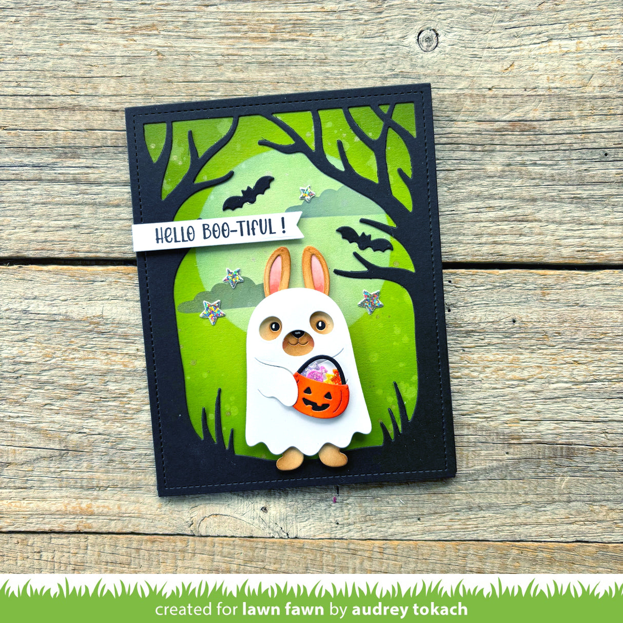 Halloween-themed card with a cartoon rabbit in a ghost costume on a wooden surface