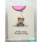 Card with a teddy bear holding a pink balloon and text 'sending caring thoughts and hugs' on a light background.