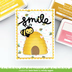 Card with bee and beehive design and 'smile' text, surrounded by ink pads and tools.