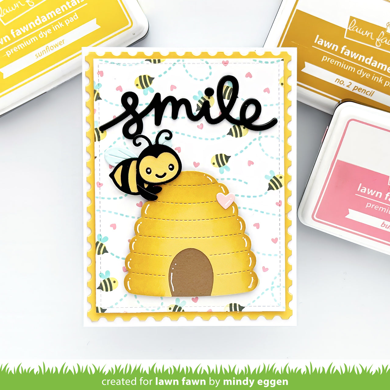 Card with bee and beehive design and 'smile' text, surrounded by ink pads and tools.