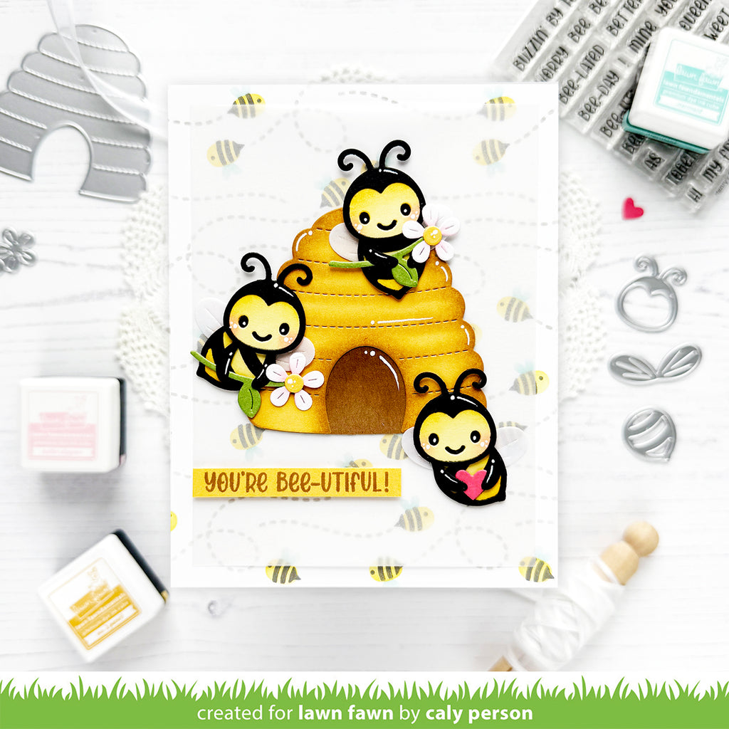 Card with cartoon bees and a beehive, featuring the text 'You're bee-utiful', surrounded by stamping supplies on a white background.
