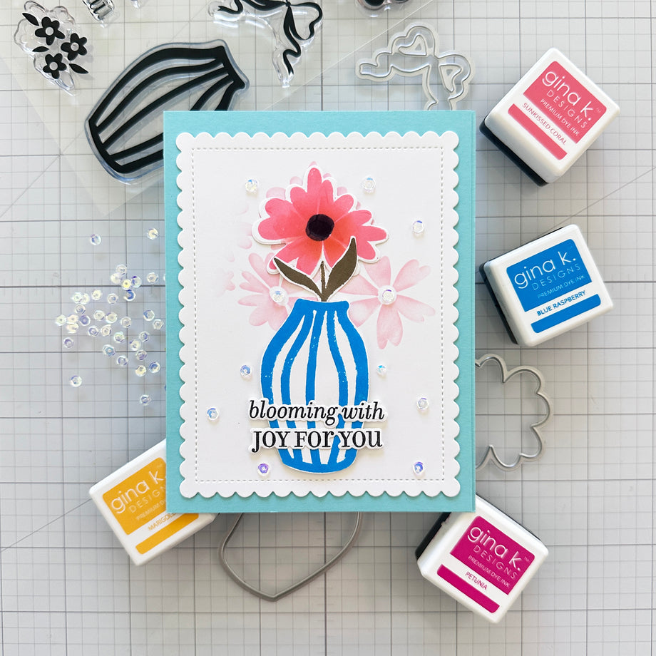 Card with floral design and 'blooming with JOY FOR YOU' text, surrounded by stamps and tools on a grid background.