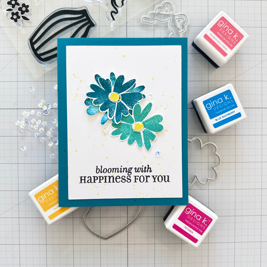 Card with floral design and text 'blooming with HAPPINESS FOR YOU' surrounded by Gina K. products on a grid background.