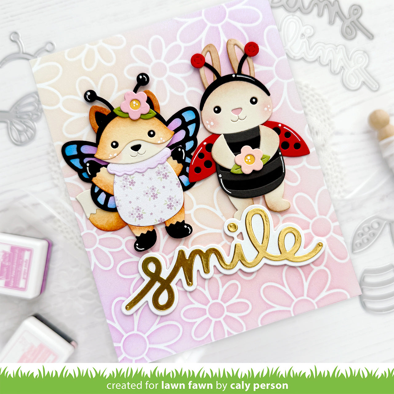 Card with fox and rabbit characters wearing insect costumes, surrounded by floral designs and the word 'smile'.