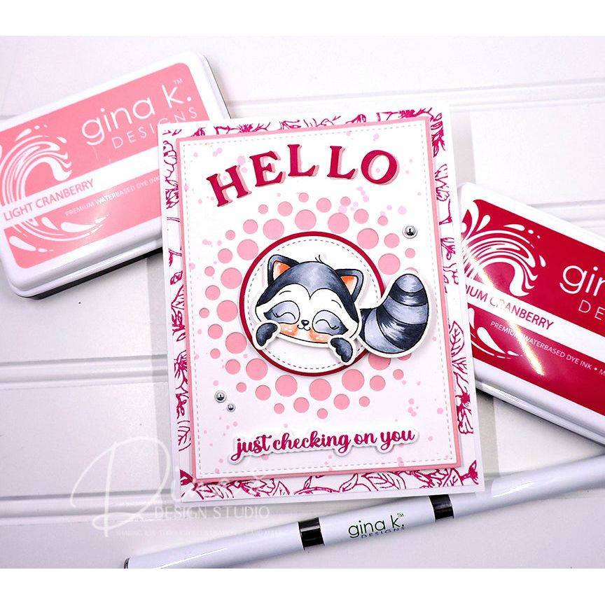 Card with raccoon illustration and 'HELLO' text, surrounded by Gina K. Designs products on a white background