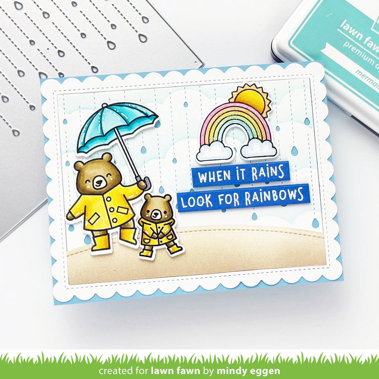 Card with two bears in raincoats and umbrellas, rainbow, and sun with text 'When it rains look for rainbows'.
