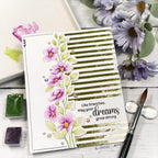 Decorative card with floral design and motivational quote on a wooden surface with flowers and art supplies.