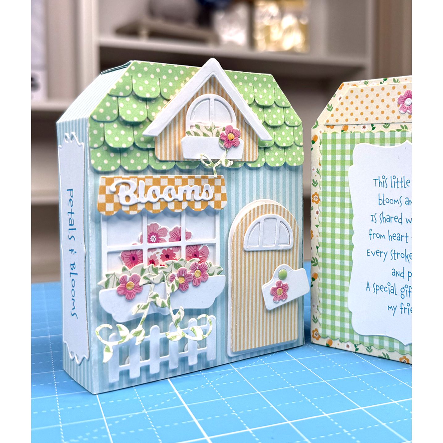 Decorative house-shaped card with floral design on a blue cutting mat.