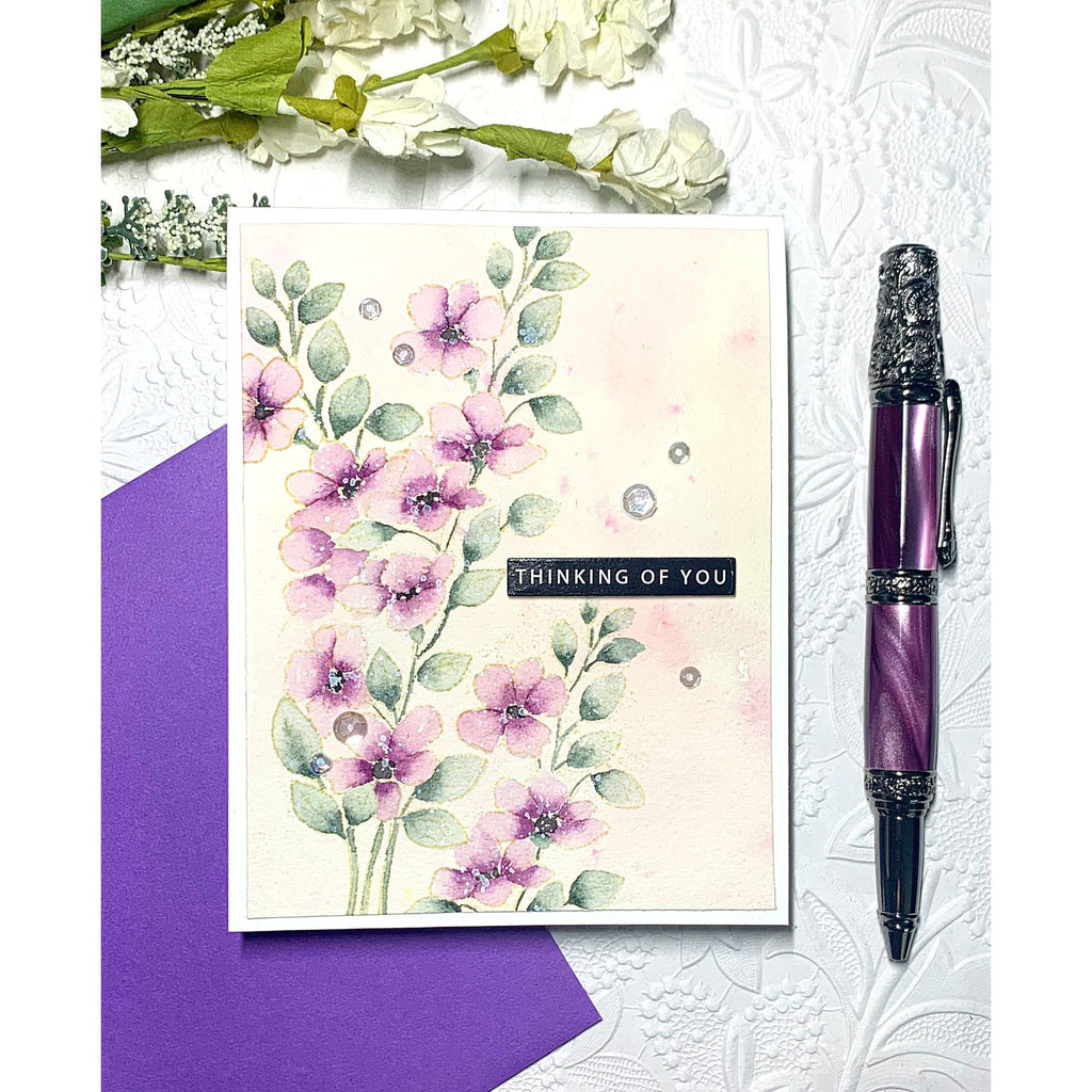 Floral card with 'Thinking of You' message, purple pen, and purple envelope on textured white background